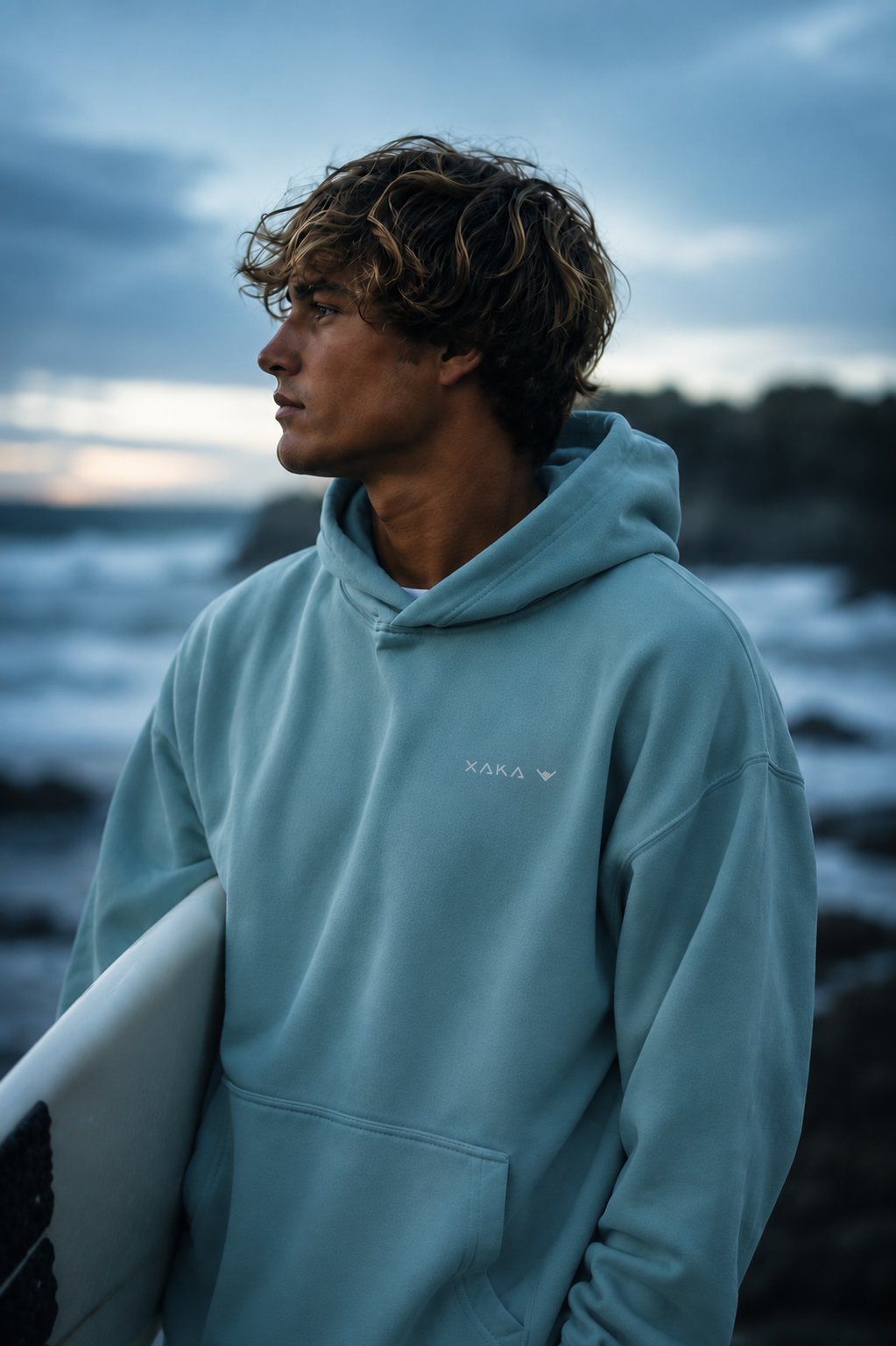 Surfer wearing a XAKA hoodie and holding a surfboard